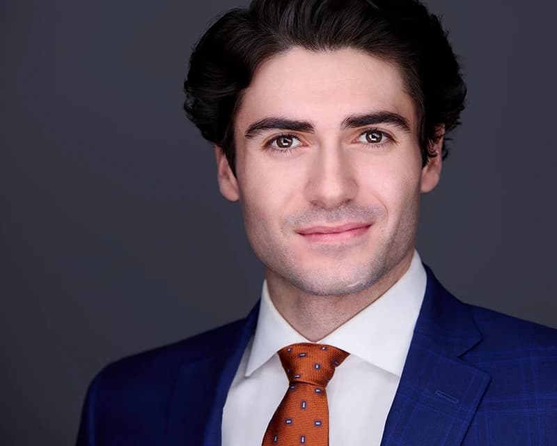 Professional headshot of man in navy plaid suit with patterned tie