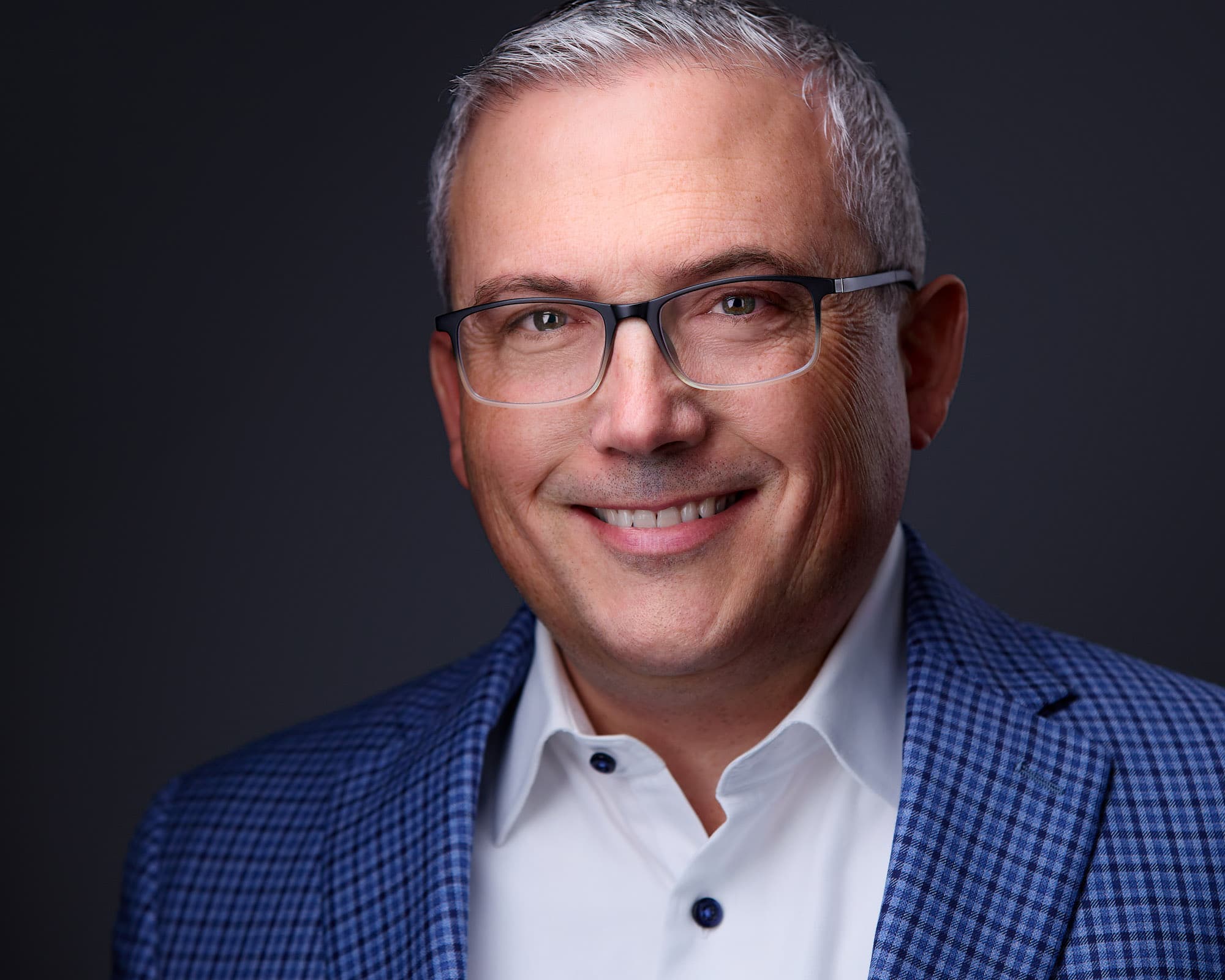 Corporate headshot of man with glasses and blue checkered blazer