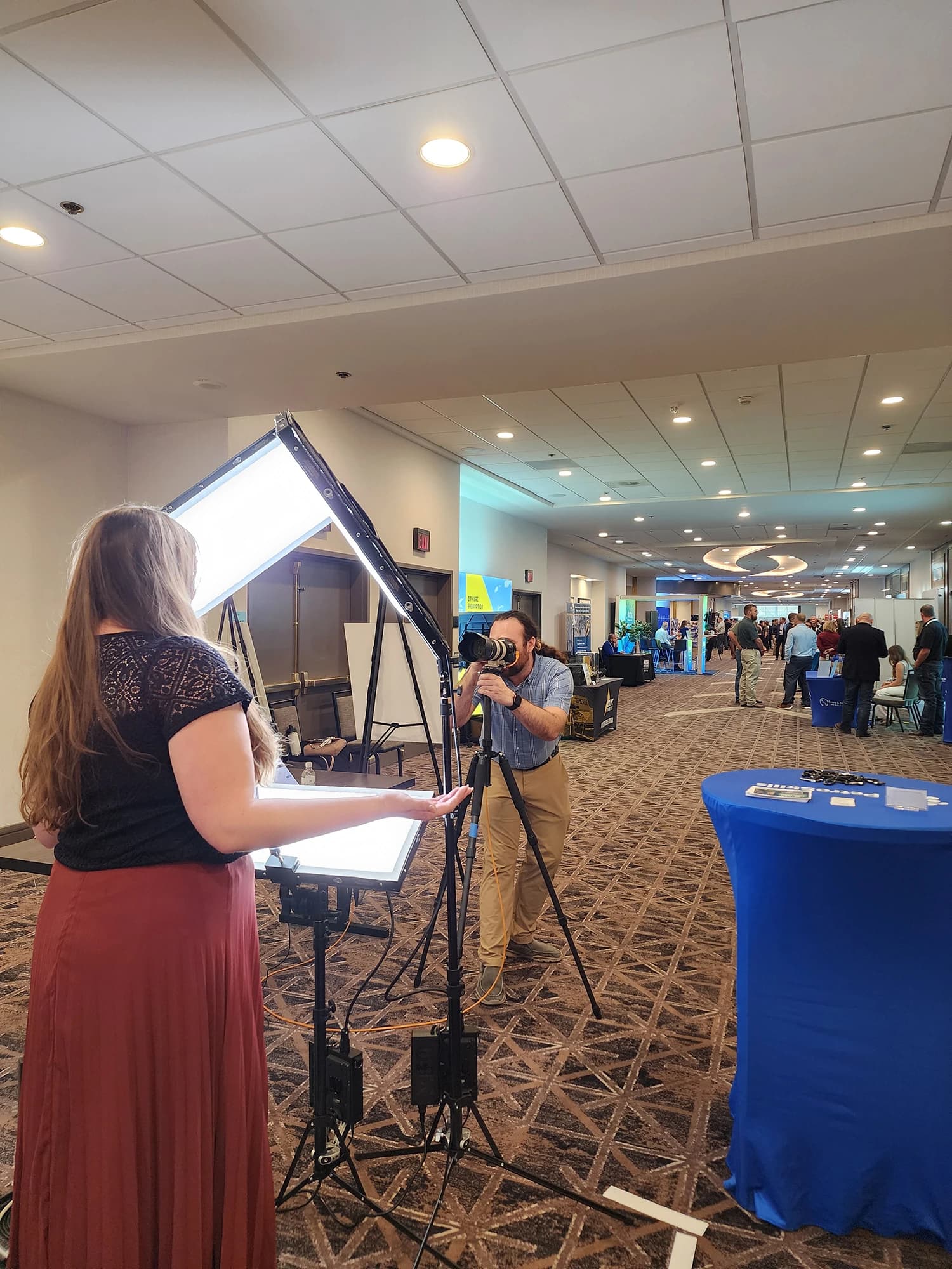 Headshot booth set up in a hotel convention corridor, photographer shooting an attendee under studio lighting with exhibitor booths behind